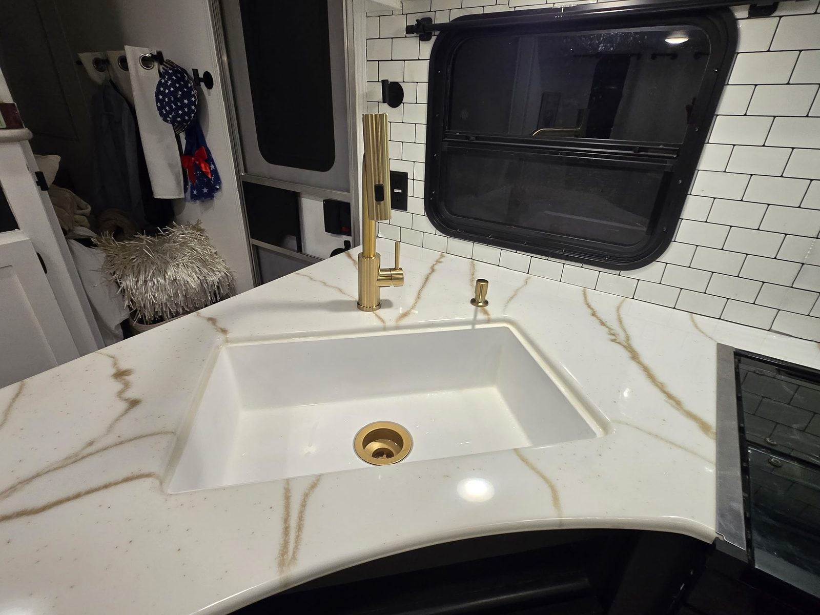 Curved RV sink counter with white and gold veining and gold fixtures.