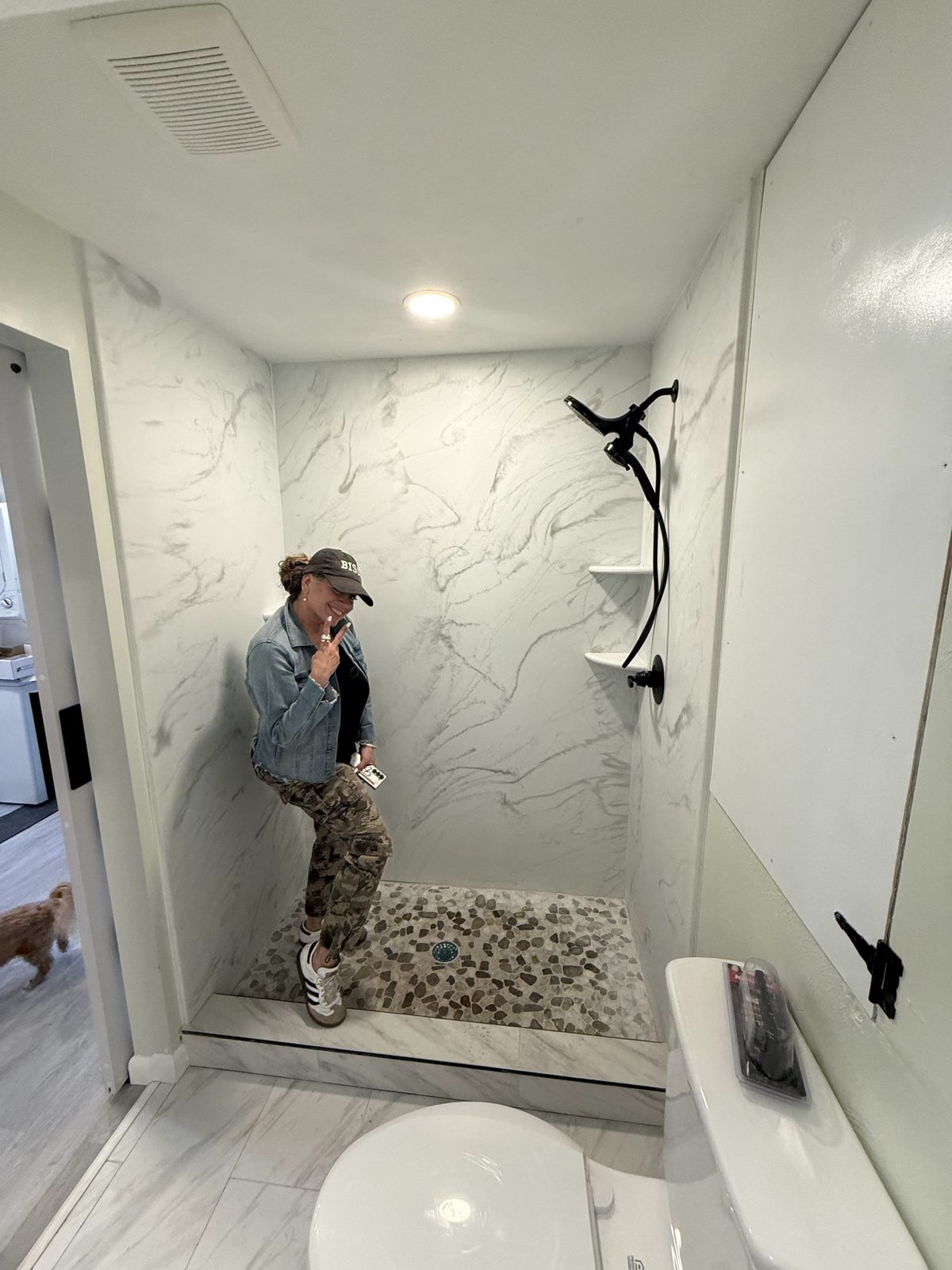 Completed marble-look shower with pebble floor and black fixtures, with a visitor posing inside.